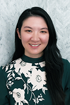 Person with long dark hair wearing a green floral blouse against a marble background.