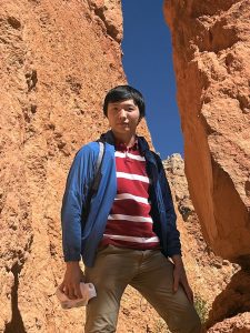 Person in a striped shirt and blue jacket standing between tall rocky formations.