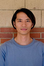 Person in blue t-shirt standing against a brick wall.